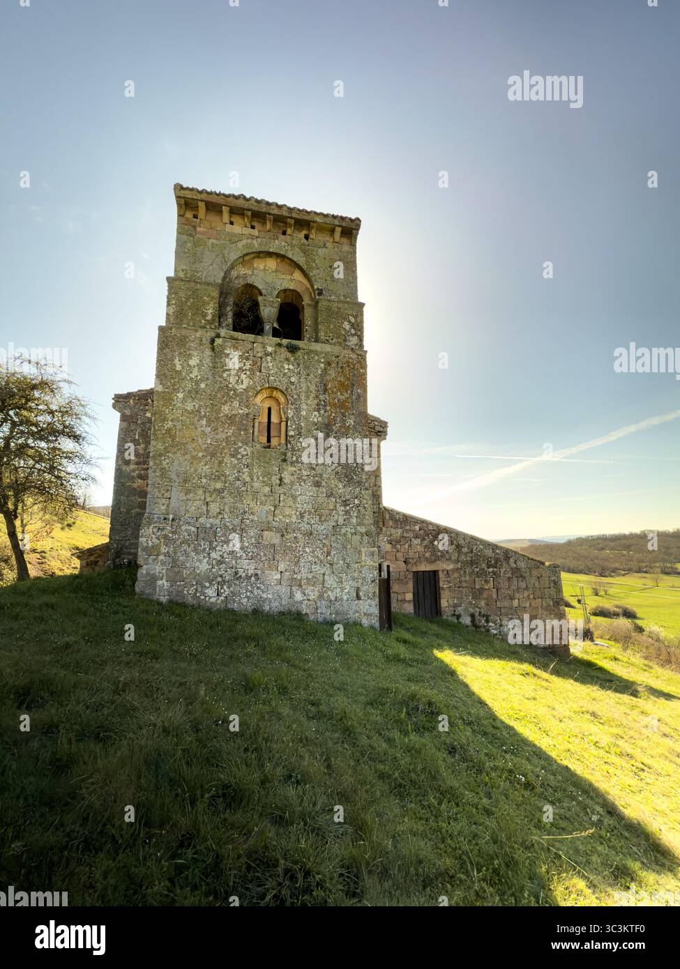 Storica chiesa romanica con pareti in pietra, tetto in piastrelle rosse e campanile annidato nella campagna di Palencia. Foto Stock
