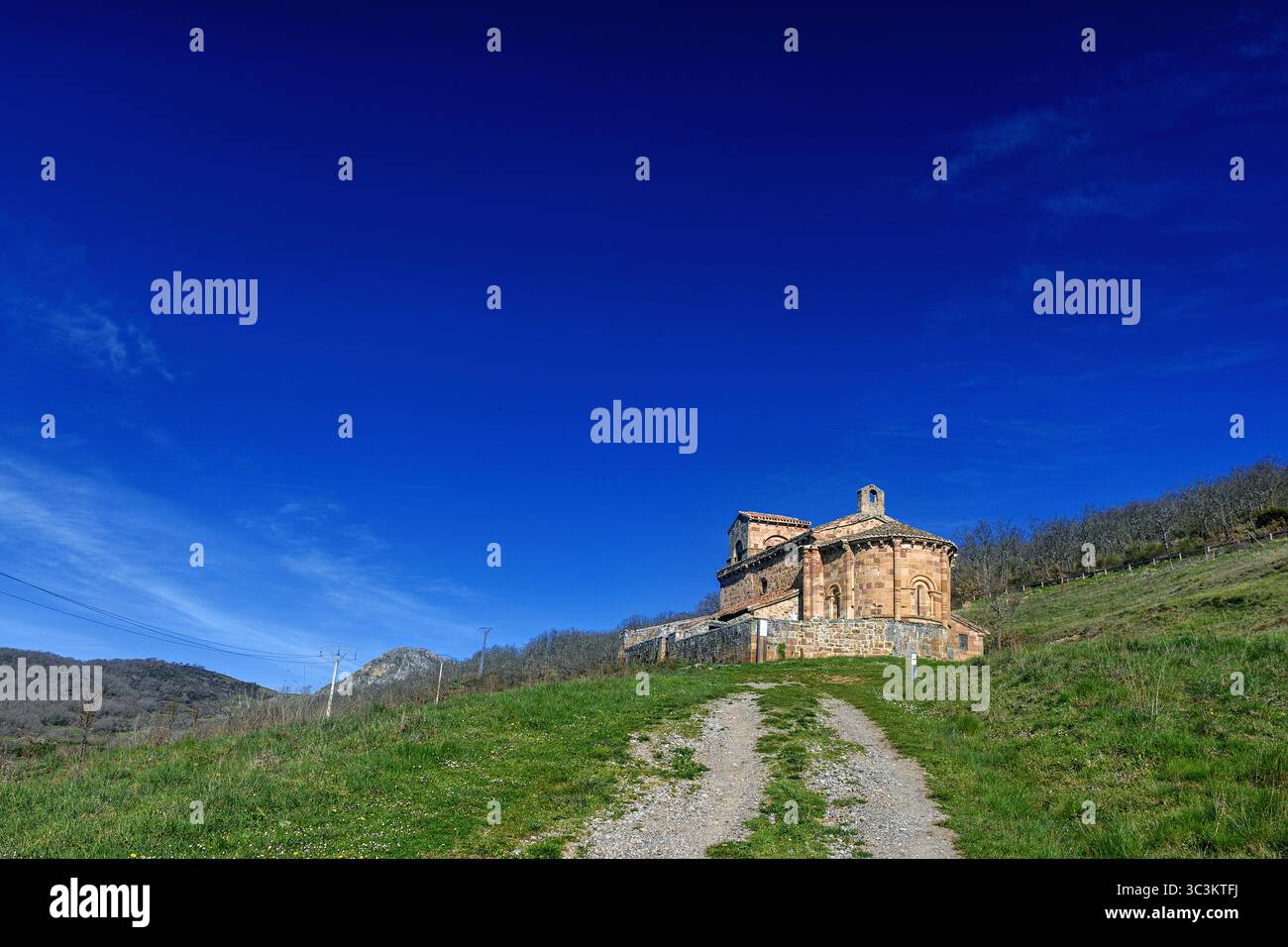 Storica chiesa romanica con pareti in pietra, tetto in piastrelle rosse e campanile annidato nella campagna di Palencia. Foto Stock