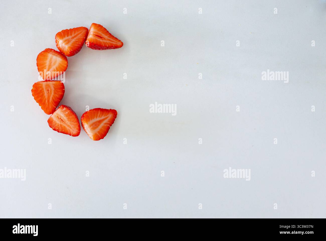 Vista dall'alto delle metà delle fragole disposte come lettera C su sfondo bianco. Concetto: Alfabeto, cibo, minimalismo, creatività Foto Stock