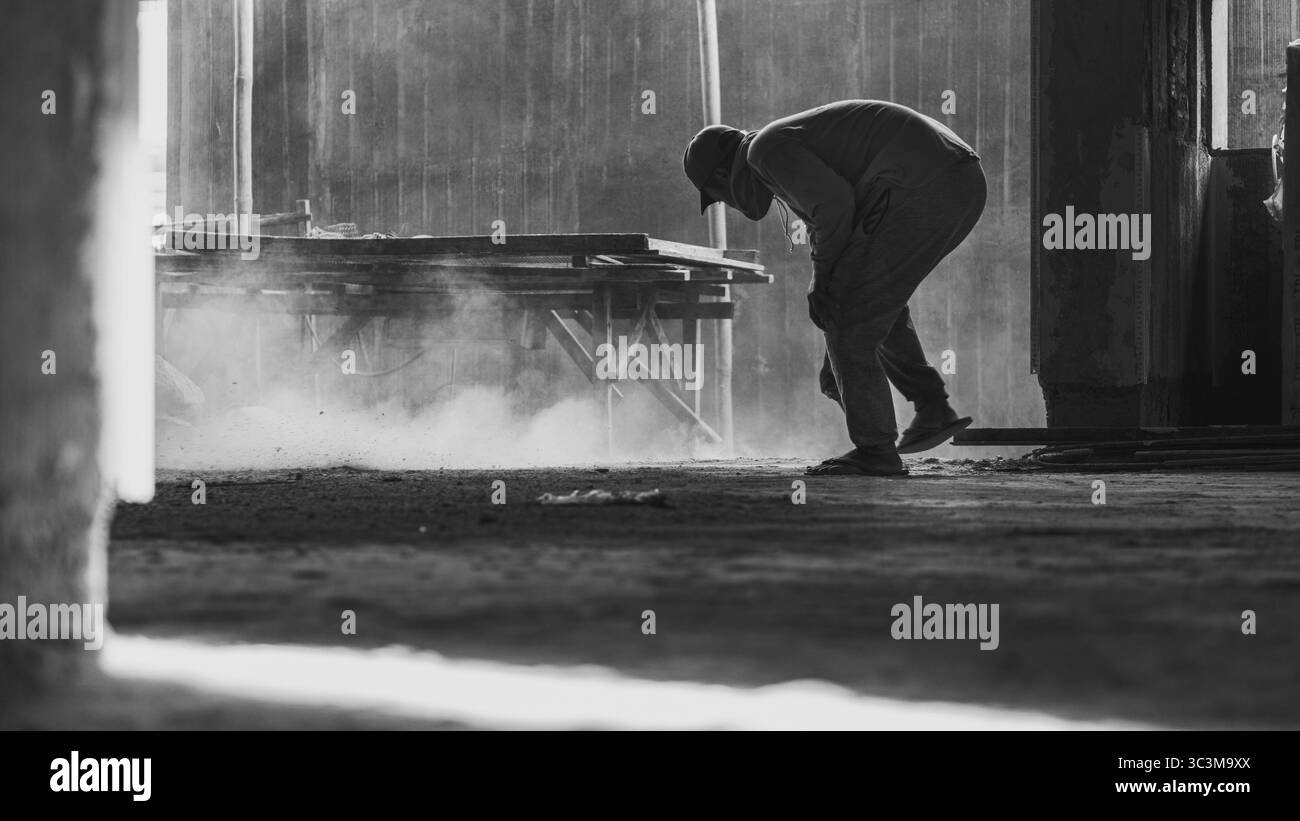 Una scopa attraversa il sito polveroso, sollevando in aria sabbia fine, catturando una disciplina tranquilla nel cuore di una zona di costruzione robusta. Foto Stock