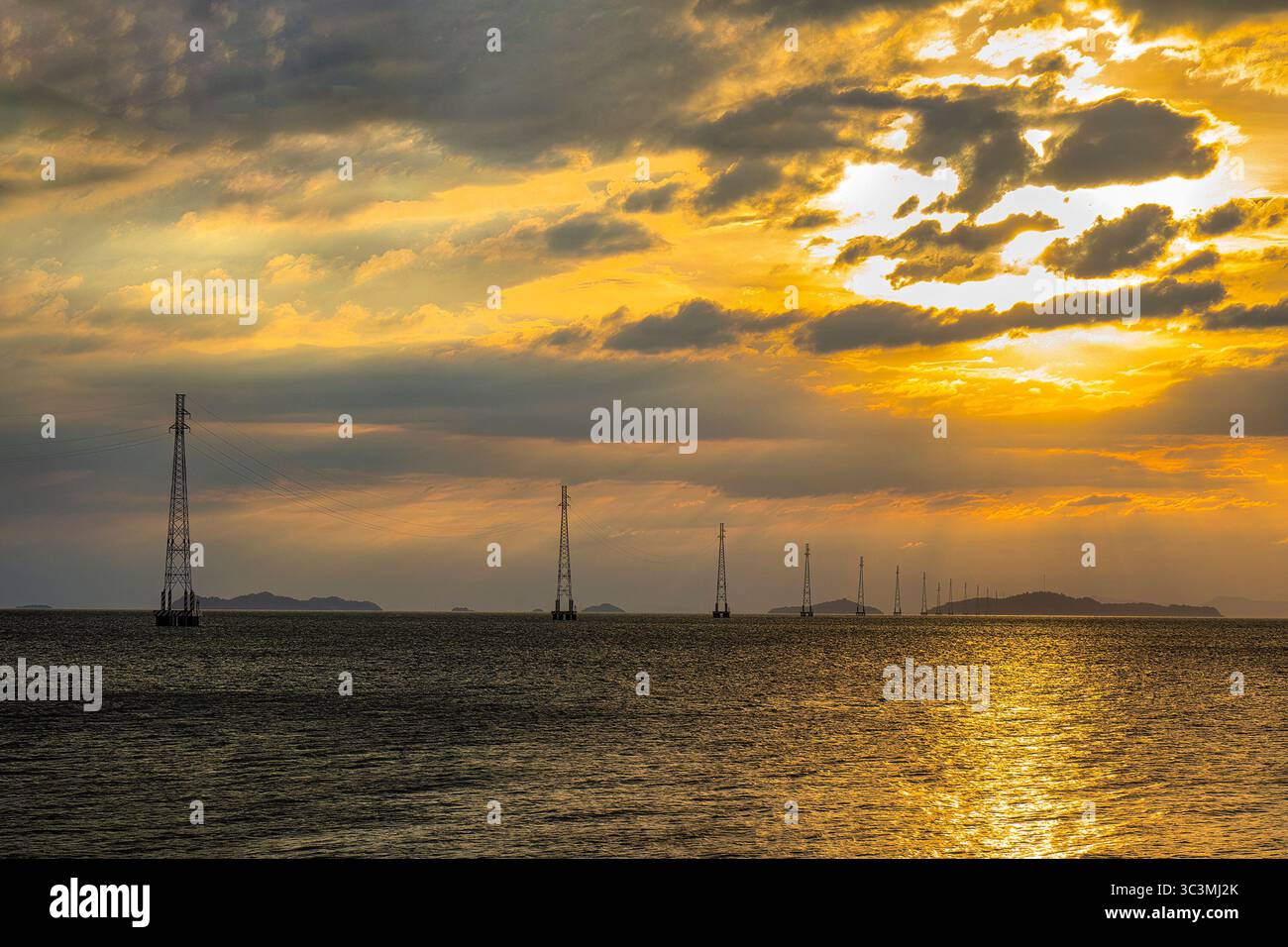 I poli elettrici del sistema di linee elettriche da ha Tien alle Isole Pirate si distinguono sulla superficie del mare nel brillante tramonto. Foto Stock