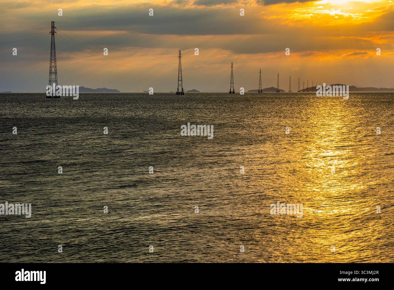 I poli elettrici del sistema di linee elettriche da ha Tien alle Isole Pirate si distinguono sulla superficie del mare nel brillante tramonto. Foto Stock