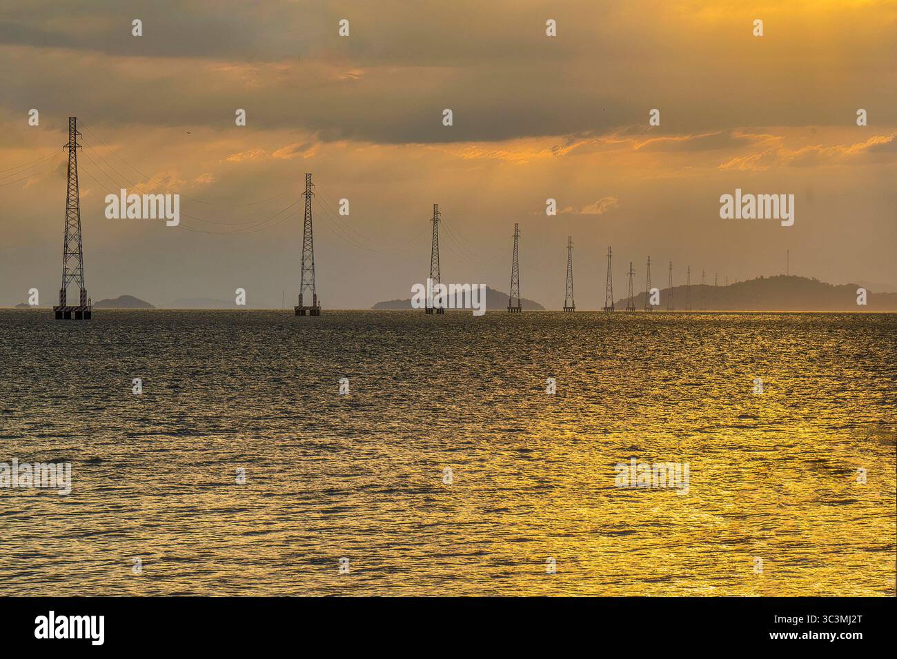 I poli elettrici del sistema di linee elettriche da ha Tien alle Isole Pirate si distinguono sulla superficie del mare nel brillante tramonto. Foto Stock
