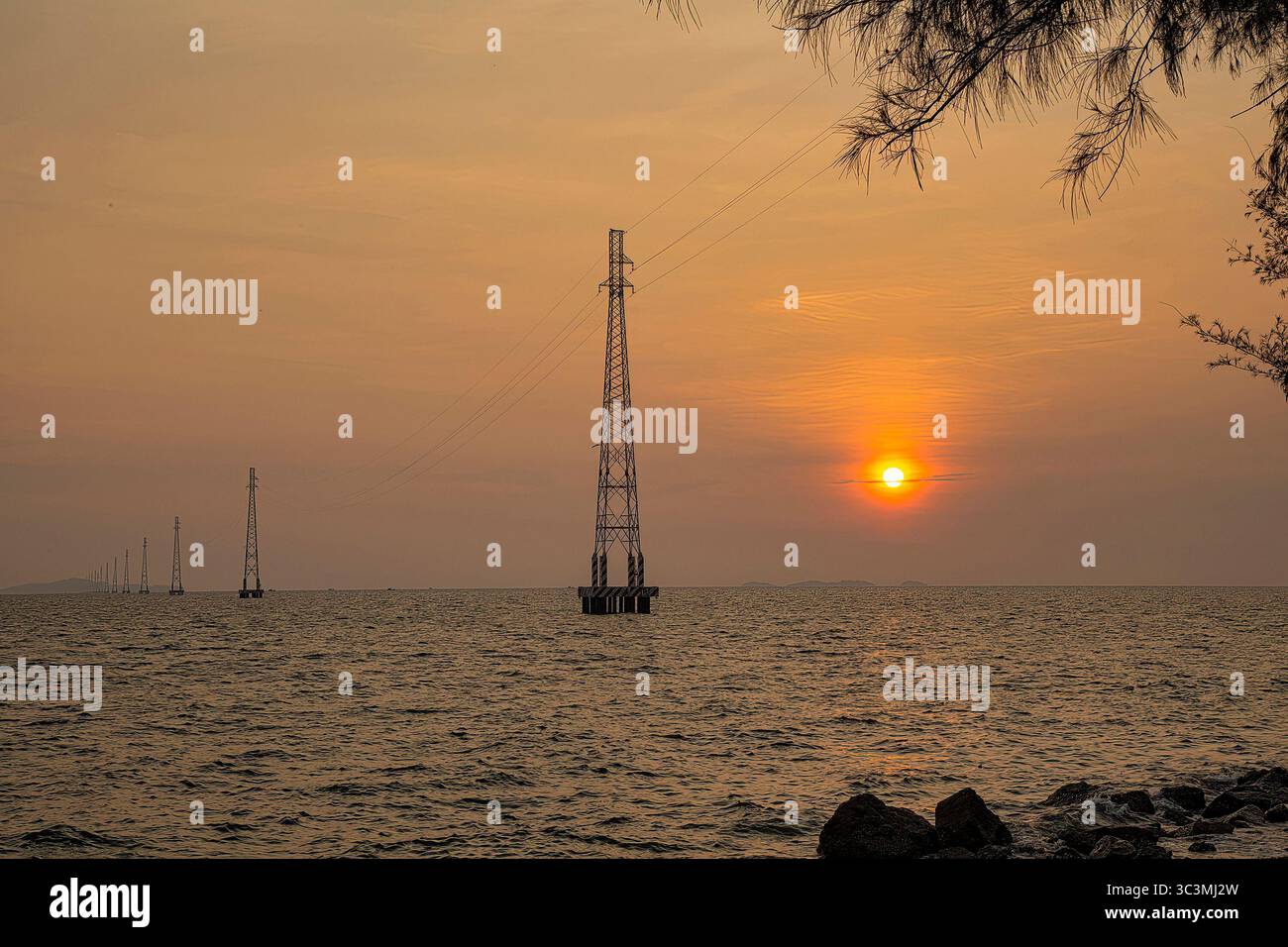 I poli elettrici del sistema di linee elettriche da ha Tien alle Isole Pirate si distinguono sulla superficie del mare nel brillante tramonto. Foto Stock