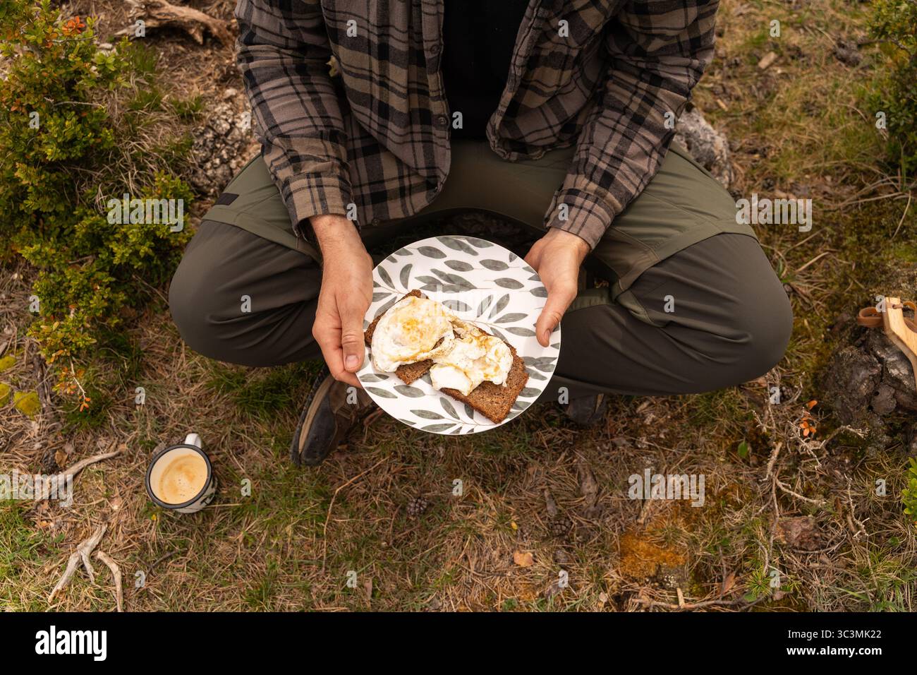 Un viaggiatore gode di una colazione rustica in natura, catturando l'essenza della vita di un furgone. Uova cucinate perfettamente sul pane tostato completano la serena atmosfera all'aperto Foto Stock
