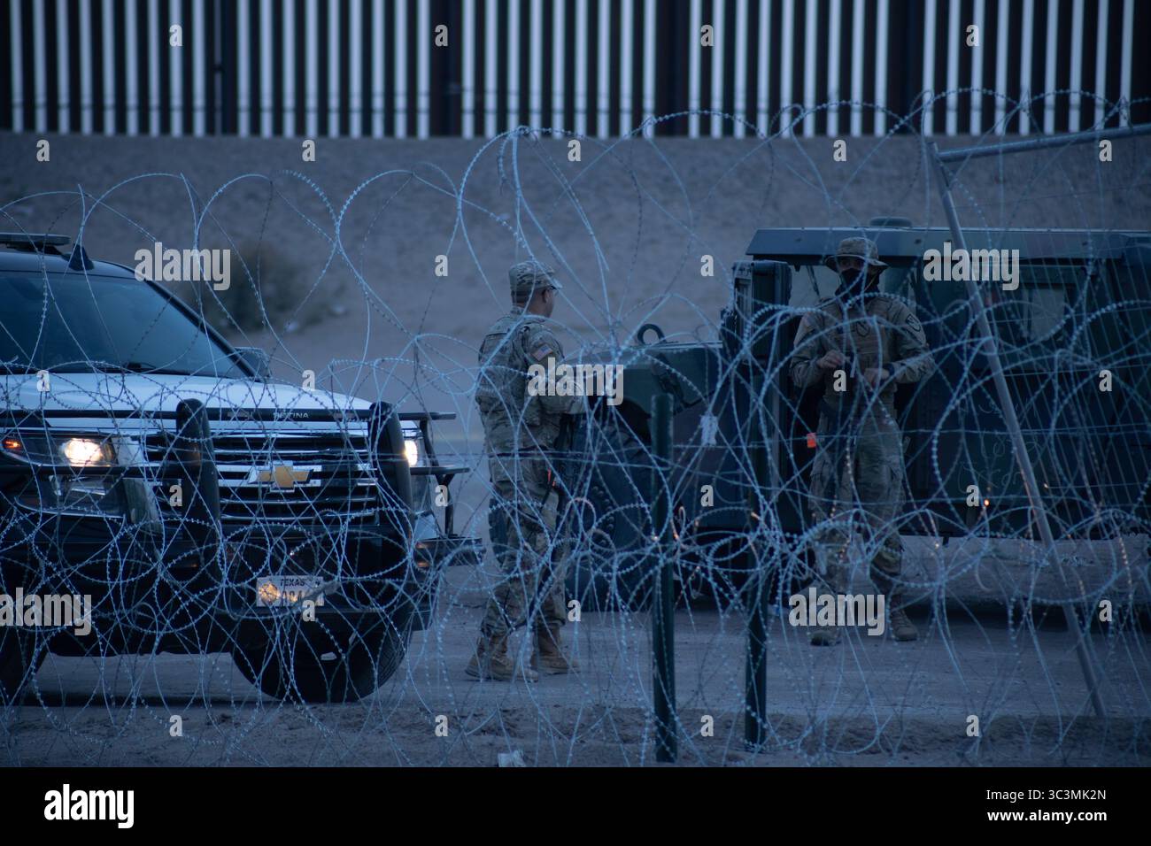 I soldati pattugliano vicino a recinzioni in filo spinato al crepuscolo lungo il confine fortificato di Ciudad Juarez, evidenziando le tensioni migratorie. Foto Stock