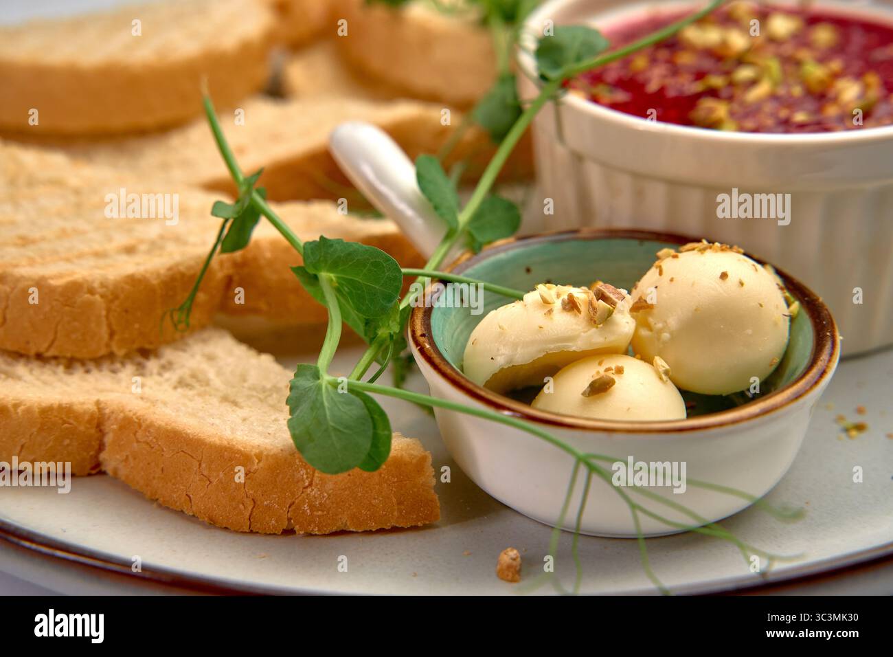 Un piatto splendidamente organizzato con pane fresco, palle di formaggio cremose, noci salate e una gustosa frutta spalmata guarnita con vegetazione per un delizioso Foto Stock