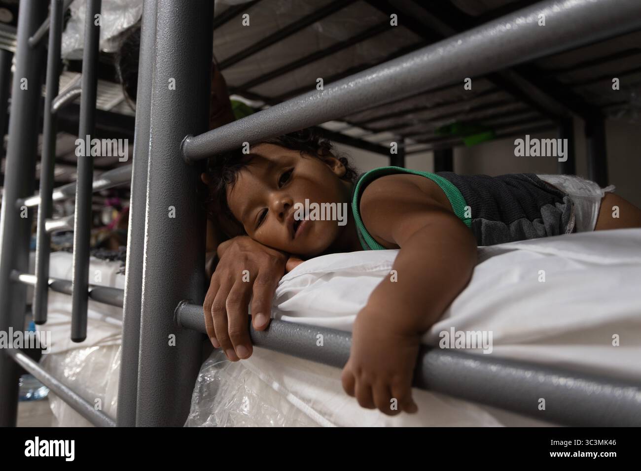 Il bambino riposa sui materassi di un rifugio di Ciudad Juarez, evidenziando i ceppi migratori. Foto Stock