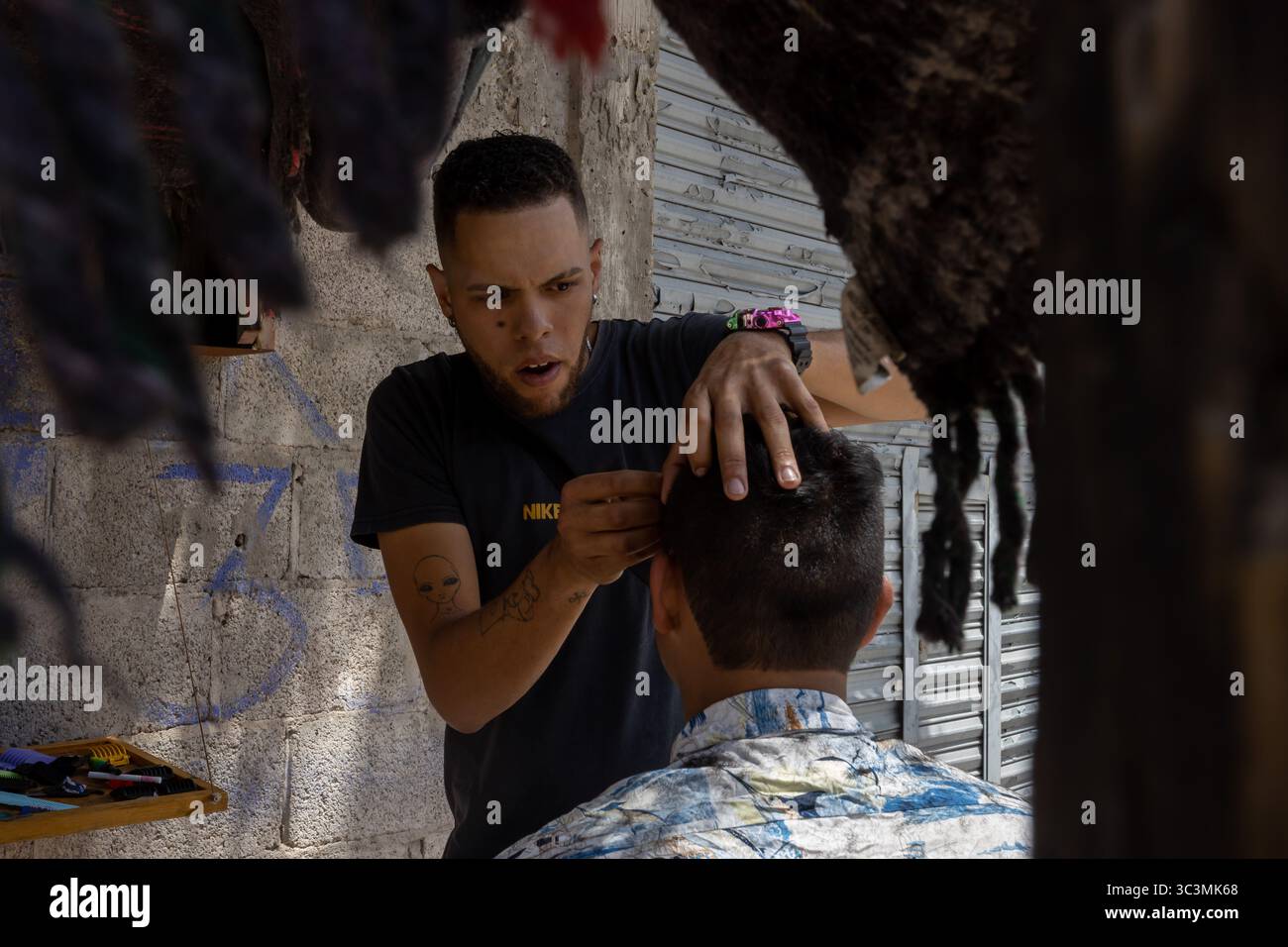 Un barbiere di Ciudad Juarez acchia i capelli tra graffiti urbani, evidenziando la resilienza locale e l'adattamento dei migranti. Foto Stock