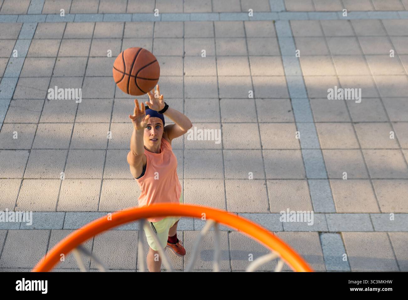 Una donna determinata con un abbigliamento sportivo fa un salto su un campo da basket all'aperto. La scena cattura la dinamica e la passione del cestino da strada Foto Stock