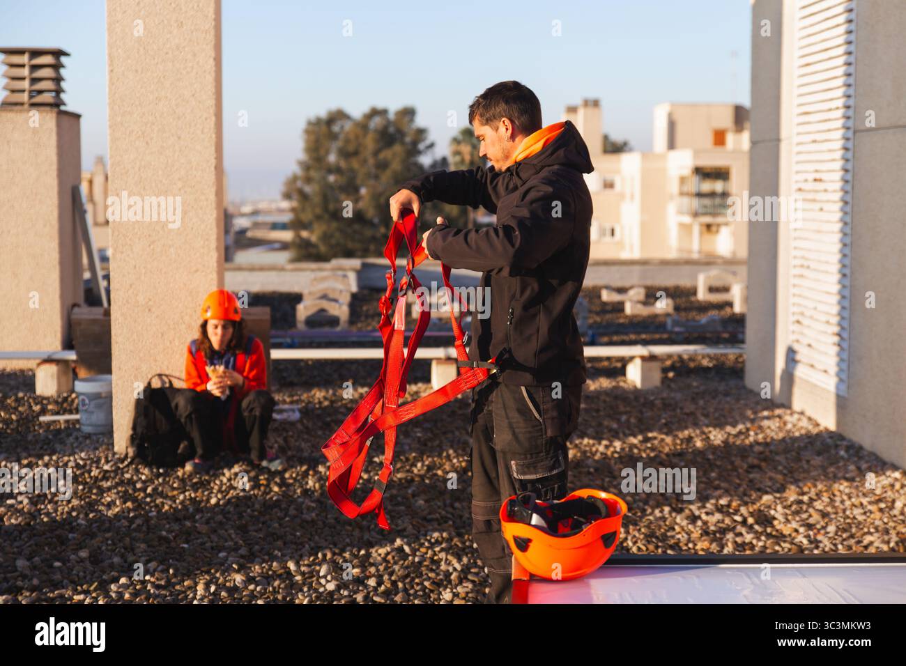 I lavoratori si preparano per l'installazione di pannelli solari sul tetto, maneggiando imbracature di sicurezza e dispositivi di protezione in cielo limpido, garantendo sicurezza ed efficienza Foto Stock
