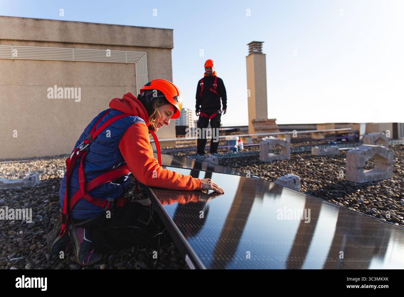 I tecnici degli attrezzi di sicurezza lavorano all'installazione di pannelli solari sul tetto di un edificio, ottimizzando la struttura per una cattura efficiente dell'energia solare Foto Stock