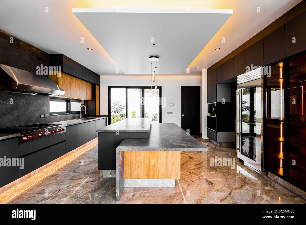 Cucina moderna ed elegante con ripiani in marmo, illuminazione sofisticata ed elettrodomestici di fascia alta. I caldi dettagli in legno completano il cabinet nero Foto Stock