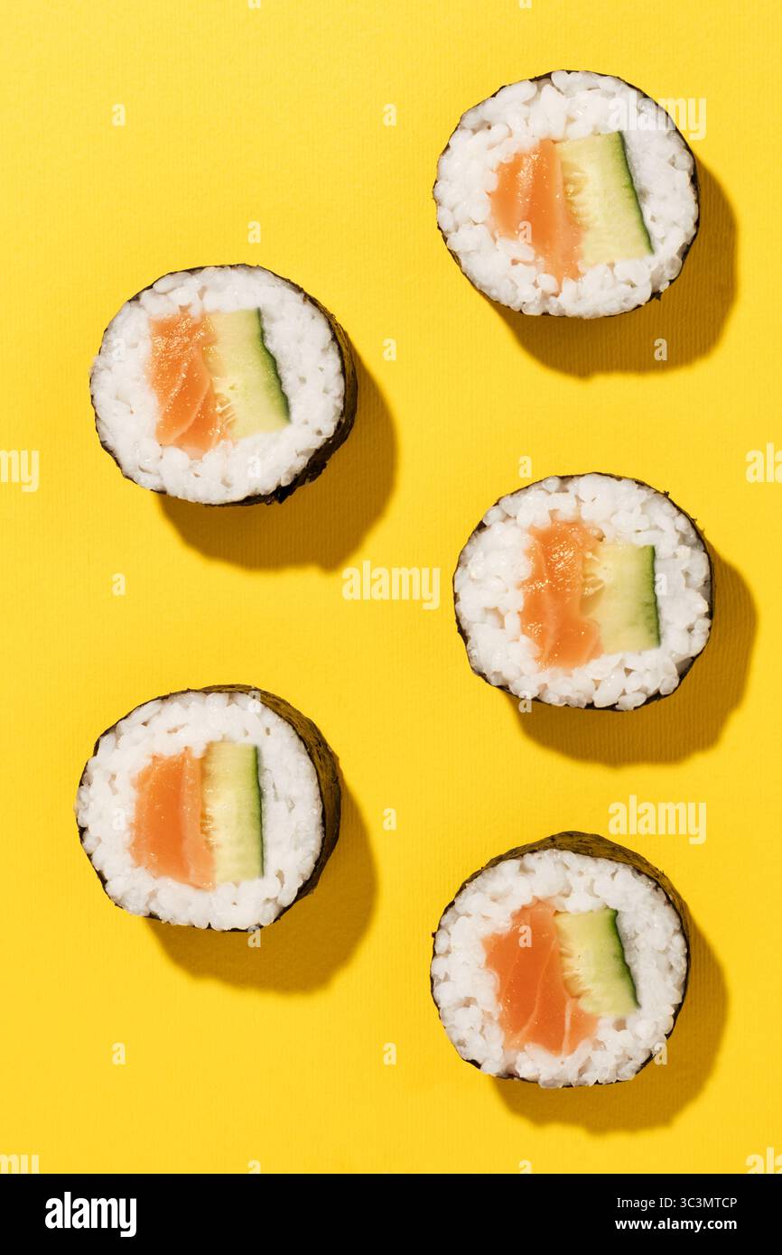 Foto in studio dall'alto di cinque sushi roll con salmone e cetriolo freschi su un vivace sfondo giallo, che presenta un'appetitosa esposizione di giapponesi Foto Stock