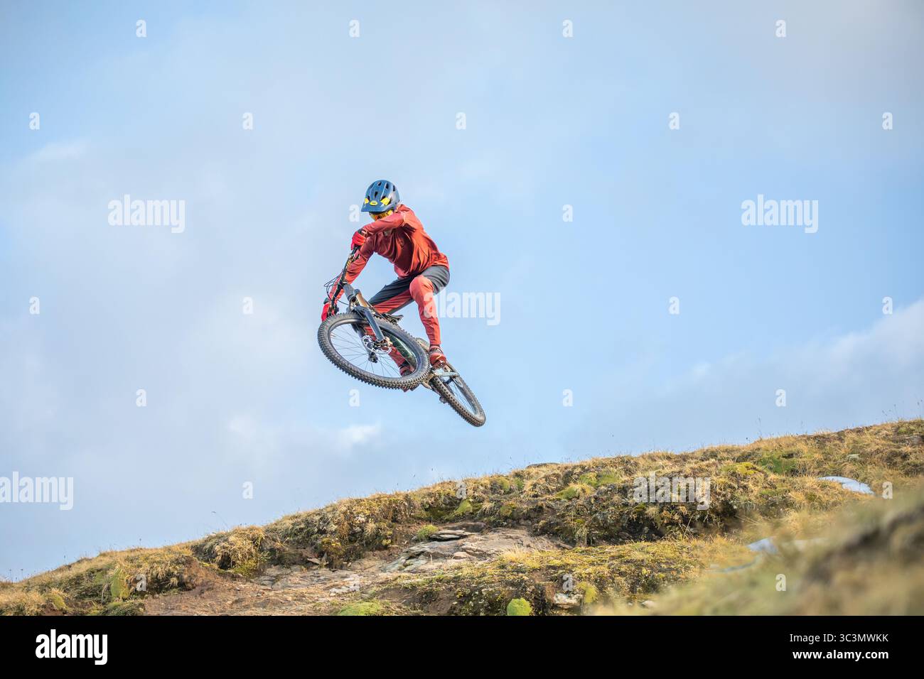 Dal basso un uomo irriconoscibile esegue una straordinaria acrobazia in mountain bike sulle Alpi, mostrando atletismo emozionante e la bellezza del r Foto Stock