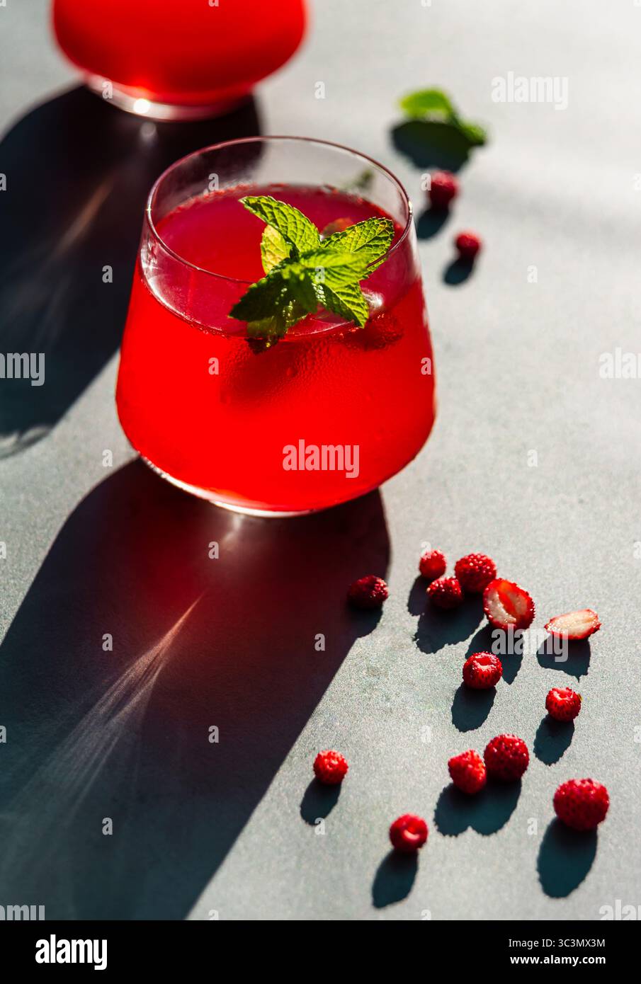 Dall'alto, un vivace e freddo tè estivo con fragole e ibisco è guarnito con foglie di menta fresche, crogiolandosi alla luce diretta del sole per un rinvigorito Foto Stock