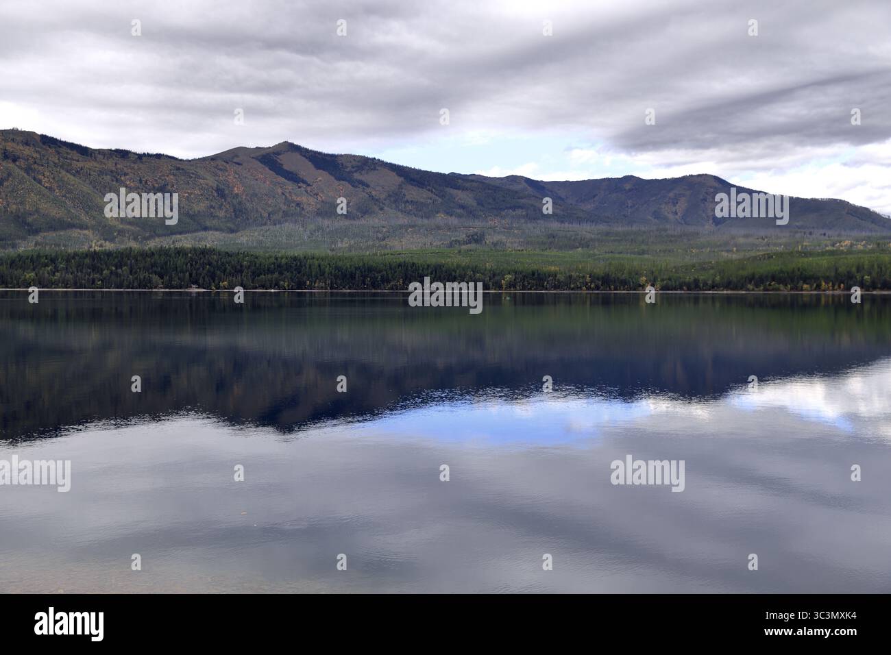 Nuvole illuminate dal sole si innalzano sopra il lago McDonald mentre le acque cristalline rispecchiano aspre vette e foreste autunnali, offrendo una tranquilla fuga nella natura selvaggia da esplorare. Foto Stock