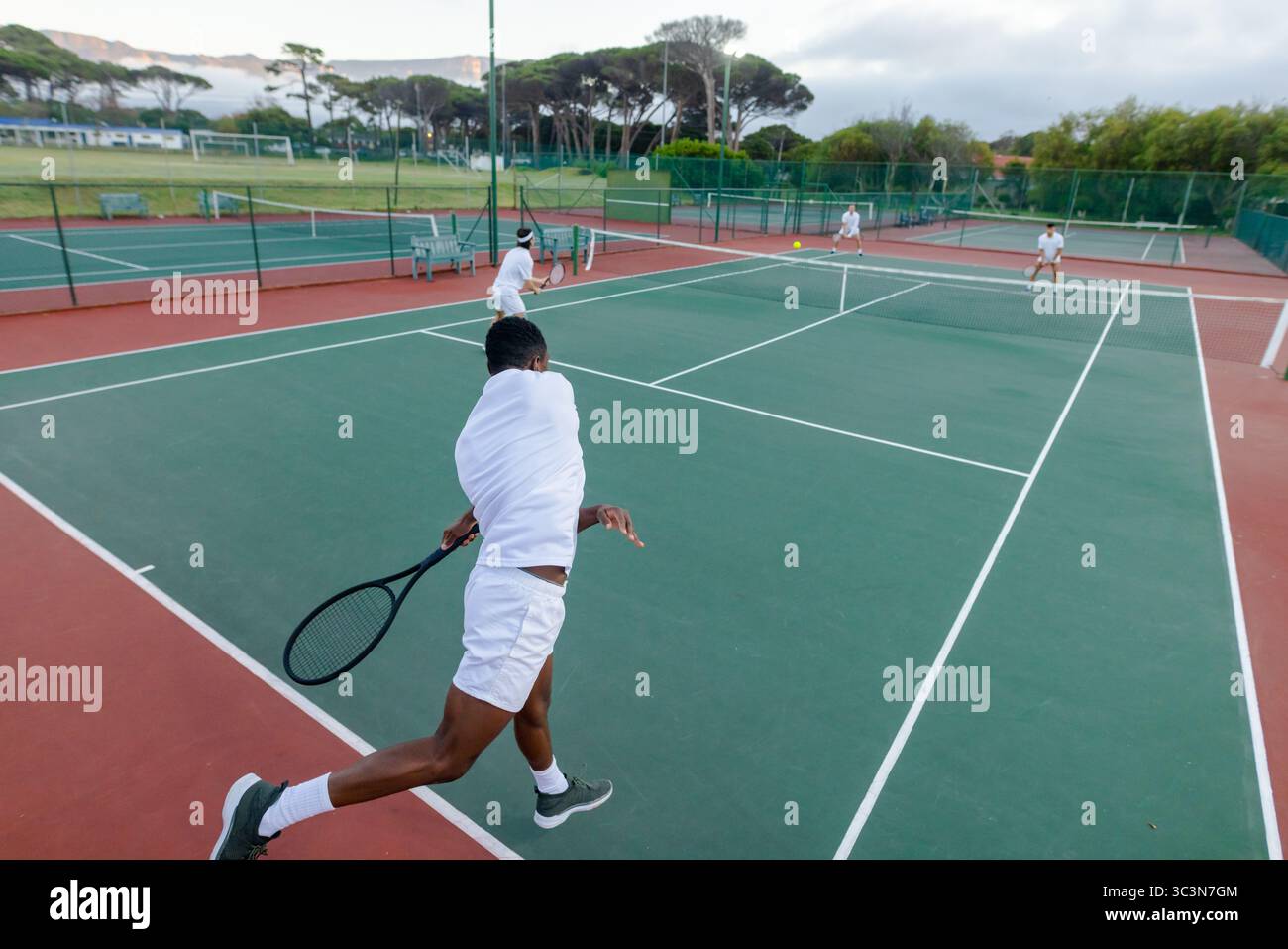 Diversi tennisti maschi competono intensamente sul campo duro all'aperto con racchette, palla e rete Foto Stock