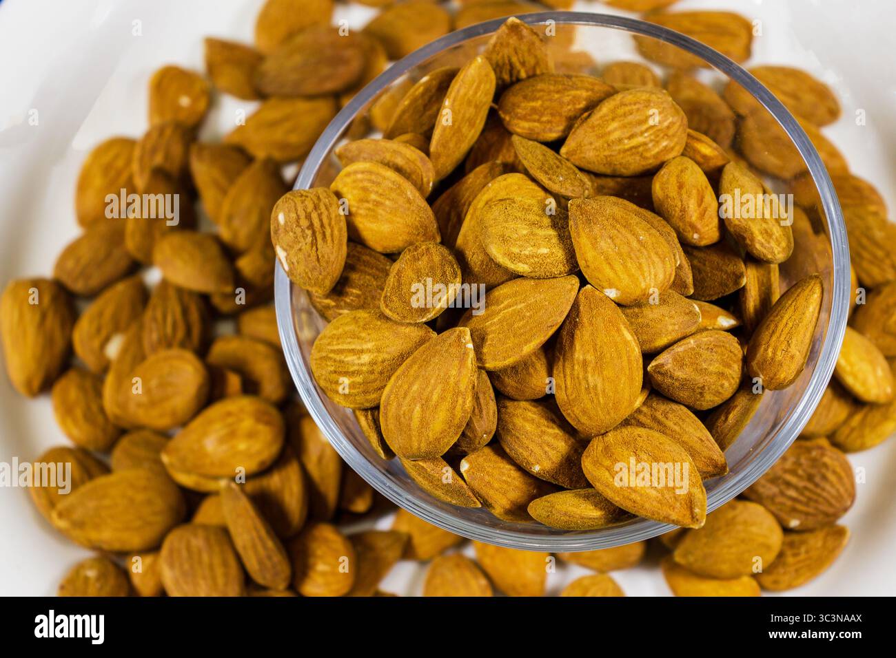 Ciotola di mandorle arrostite su una superficie bianca con vista ravvicinata Foto Stock