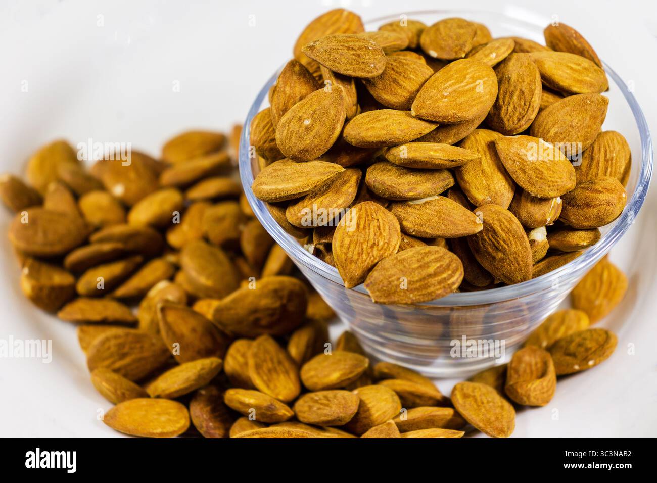 Deliziose mandorle in una ciotola di vetro circondata da dadi sparsi Foto Stock