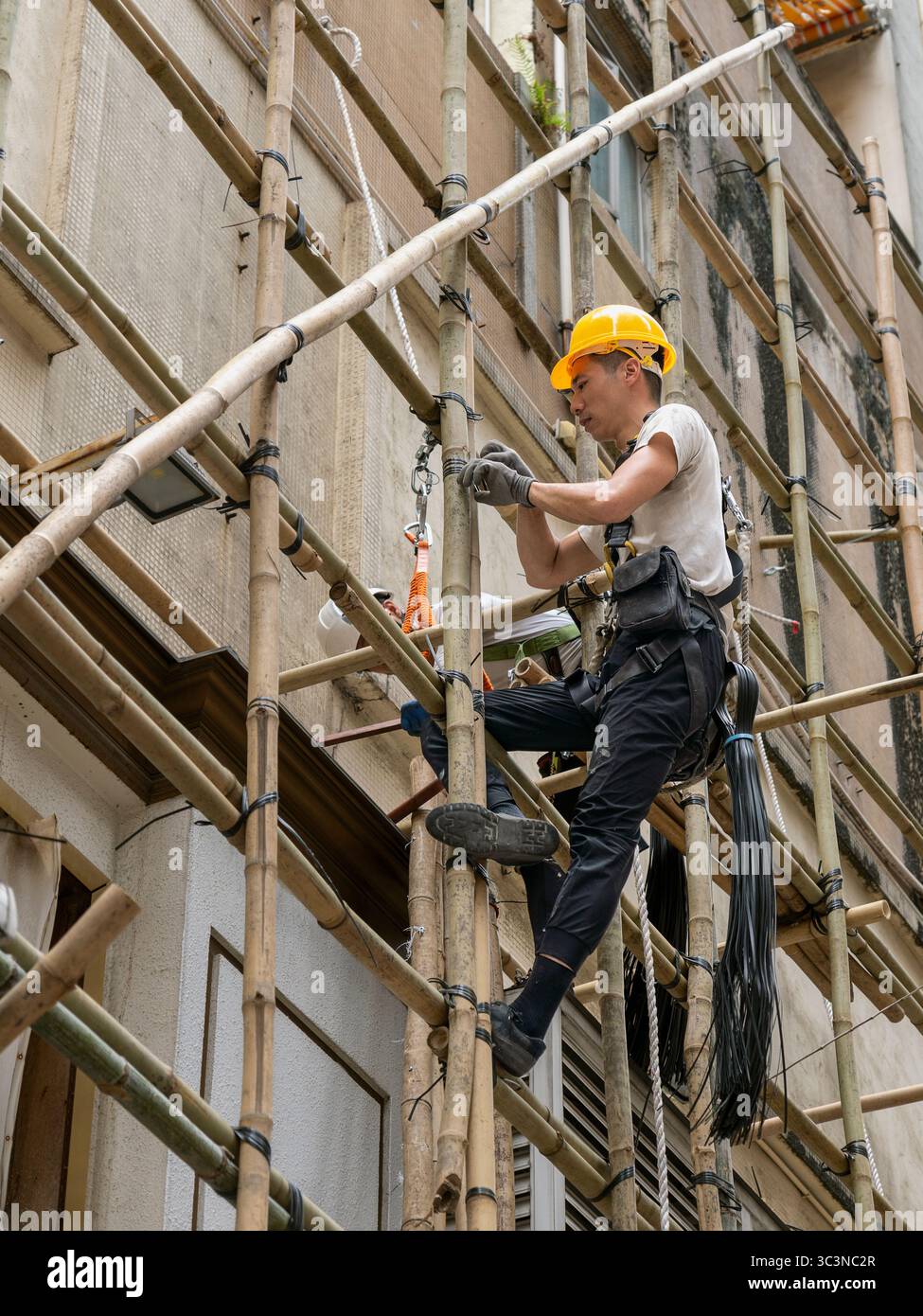 Operai edili su ponteggi in bambù in un cantiere, sviluppo urbano, casco di sicurezza, facciata di edifici, lavoro manuale. Hong Kong, Cina, Asia Foto Stock
