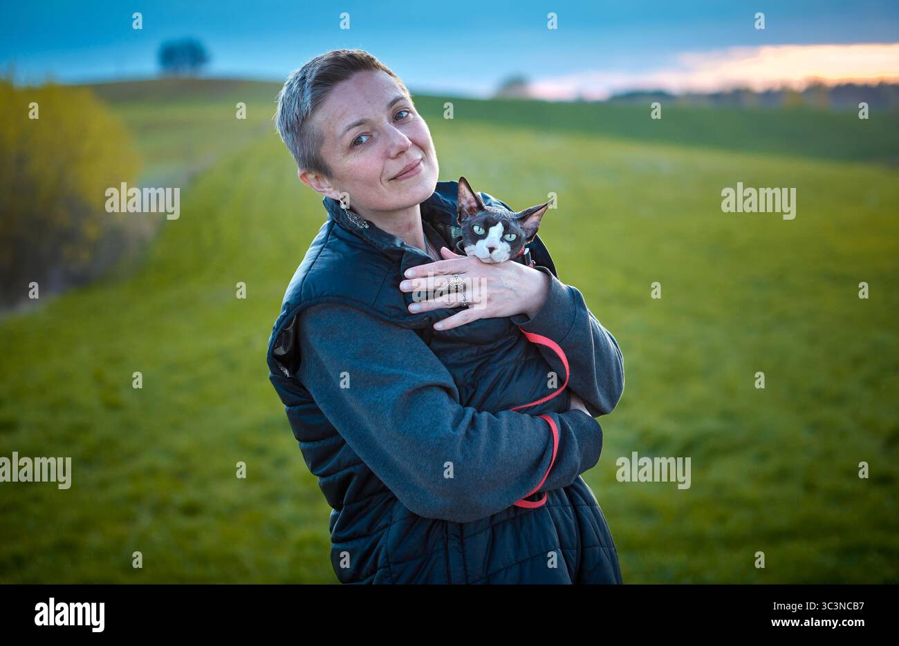 Una foto sincera dello stile di vita che mostra una donna che cammina all'aperto mentre tiene in braccio un gatto canadese Sphynx. L'immagine evidenzia l'esclusivo legame tra le due parti Foto Stock