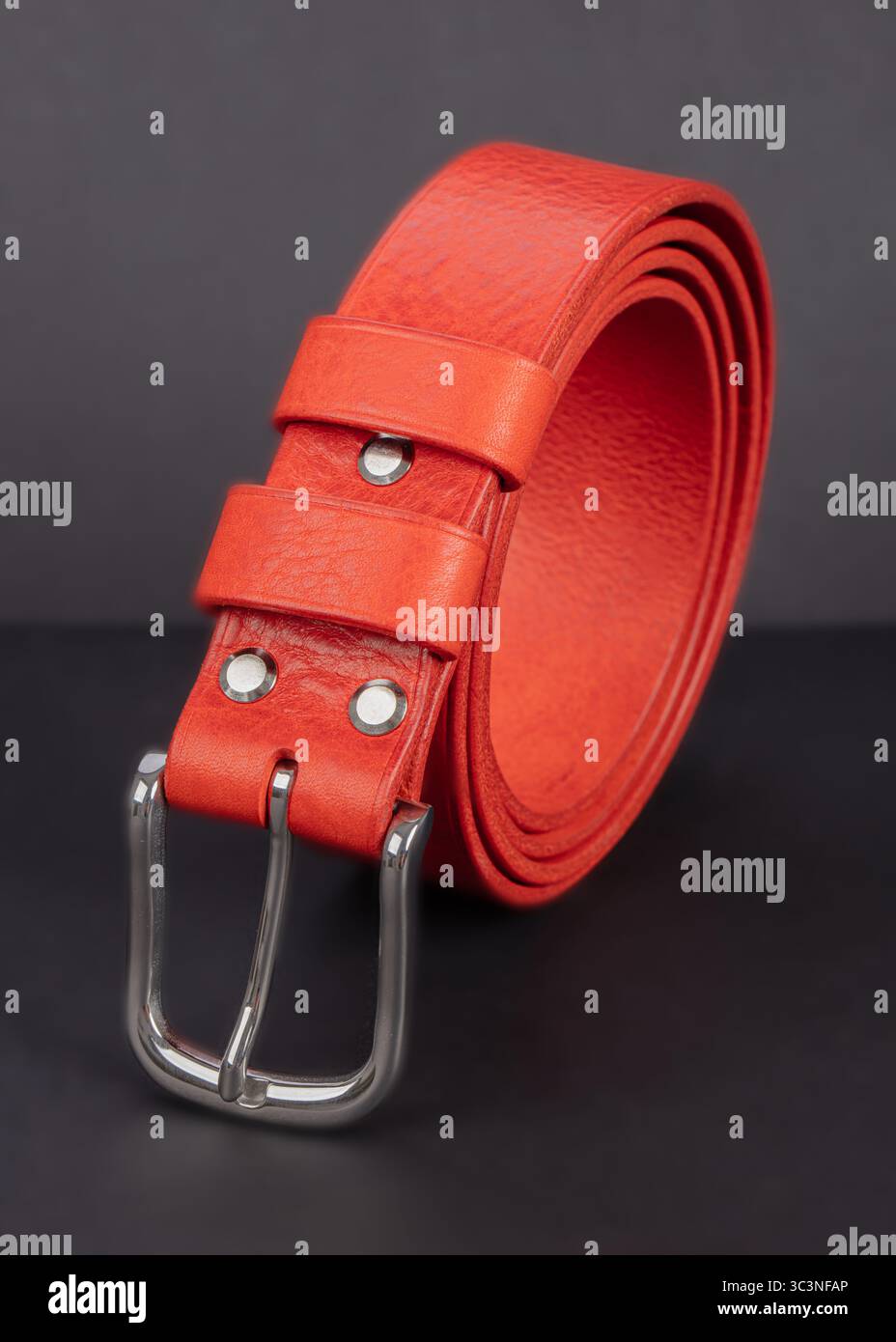 Cintura rossa in pelle con fibbie in metallo su sfondo grigio. Foto Stock