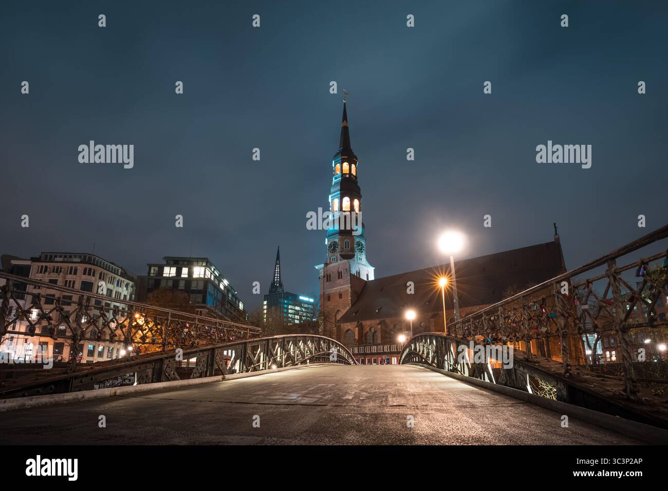 Chiesa di Santa Caterina ad Amburgo di notte con torre illuminata e cielo nuvoloso visto lungo una prospettiva di ponte Foto Stock