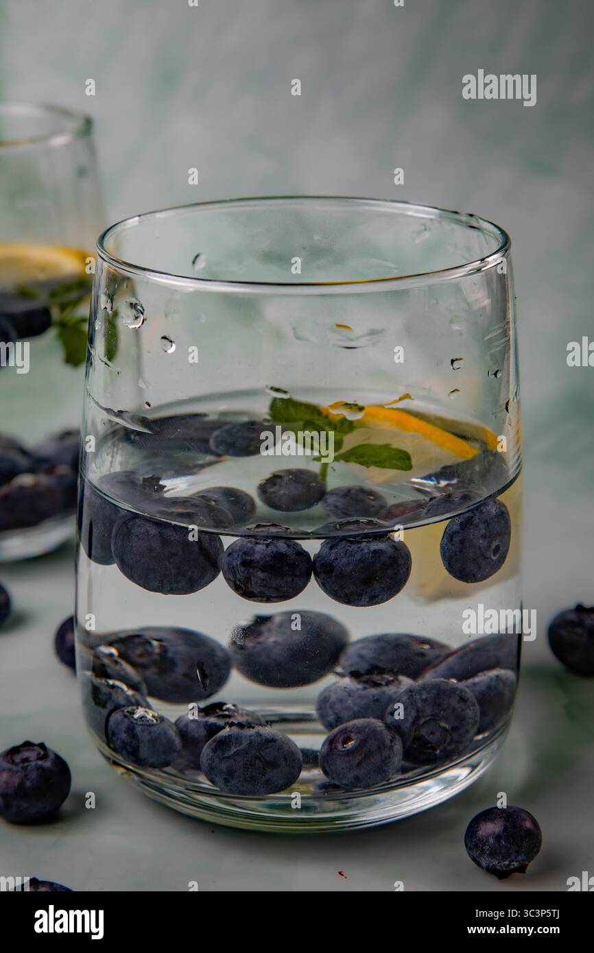 due bicchieri, con sfondo verde chiaro, con una bevanda rinfrescante fatta di acqua fredda, mirtilli, limone, menta Foto Stock