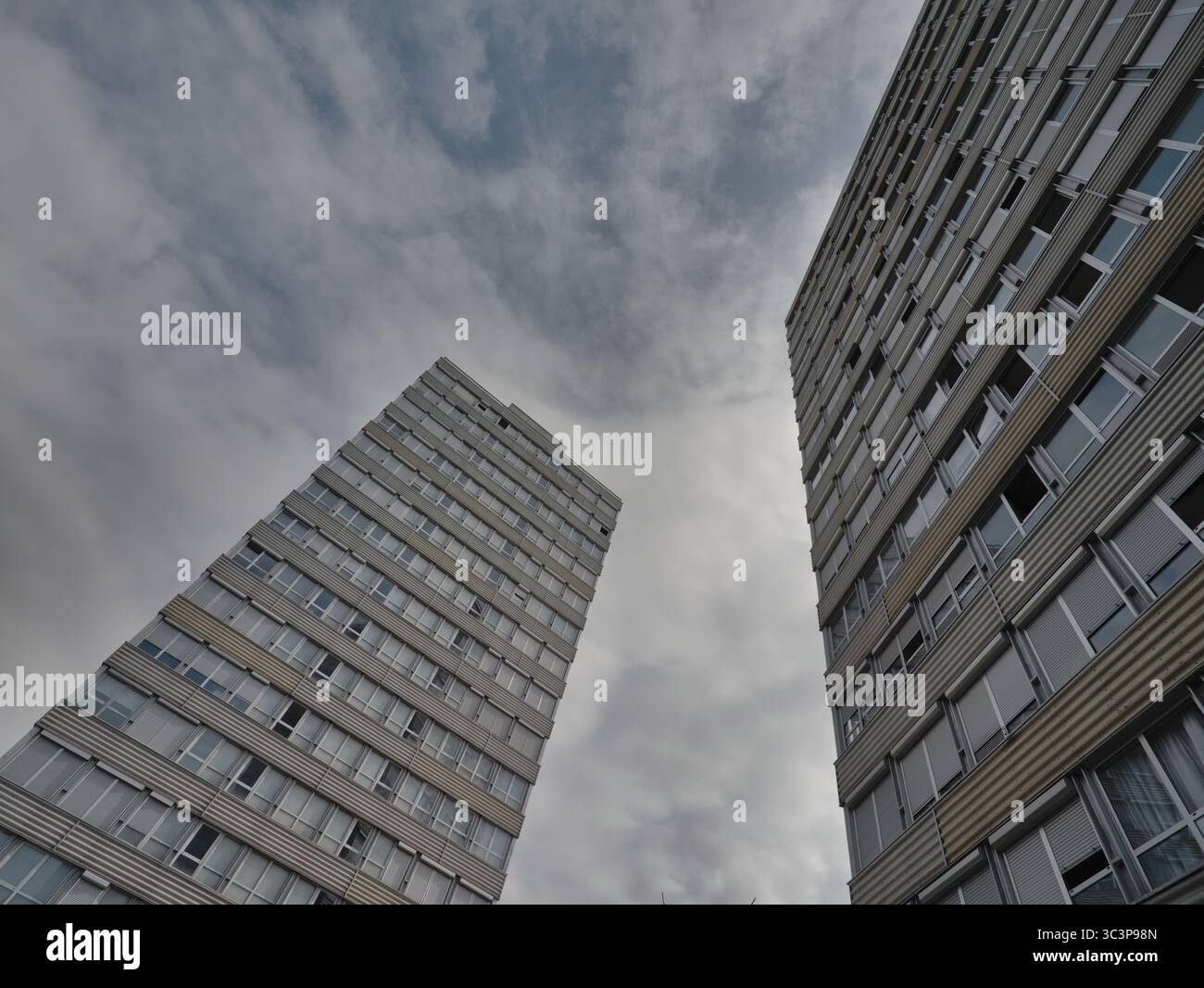 Due moderni edifici residenziali sono mostrati da un angolo verso l'alto, adagiati contro un cielo nuvoloso. Ogni struttura presenta numerose finestre, disposte in un gri Foto Stock