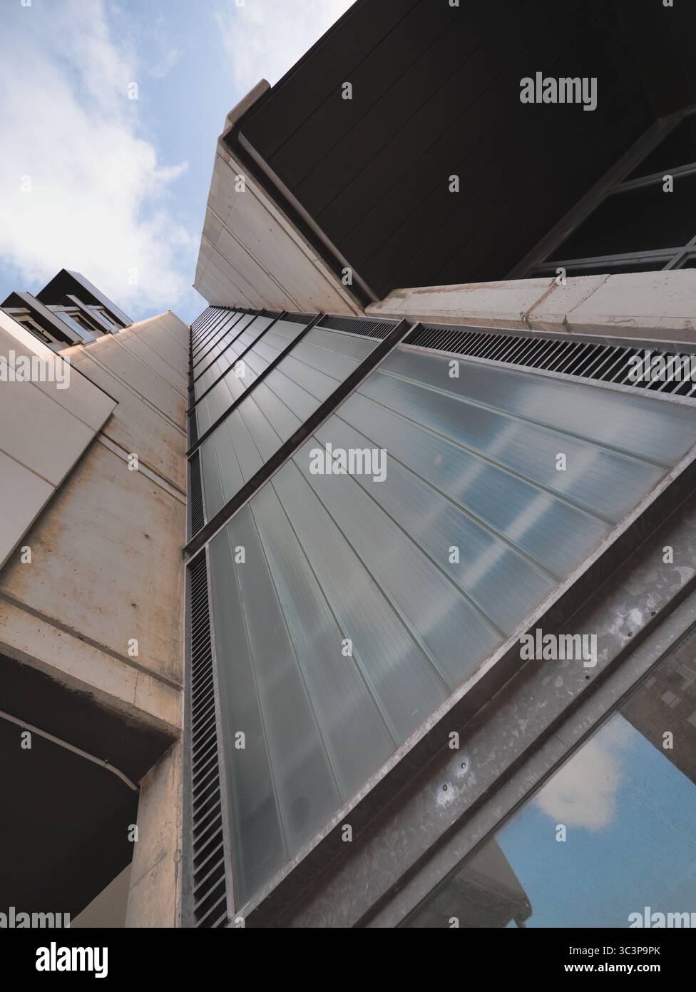 Facciata moderna dell'edificio vista dal basso, che mostra una miscela di elementi in vetro e cemento. I pannelli di vetro sono riflettenti con un disegno simile a una griglia, Foto Stock