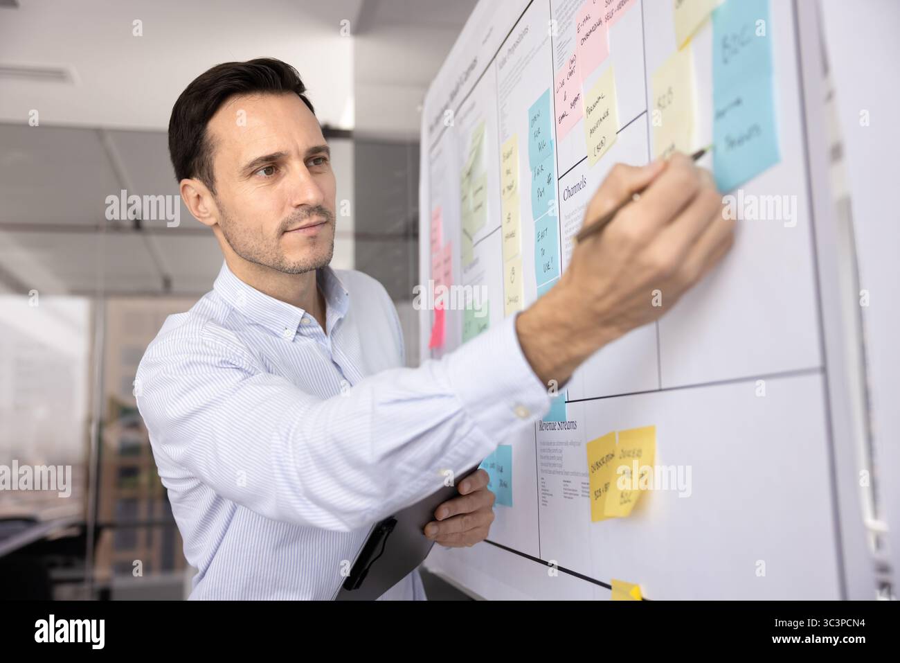 Uomo professionista serio che tiene in mano la penna, prende appunti su appunti adesivi Foto Stock