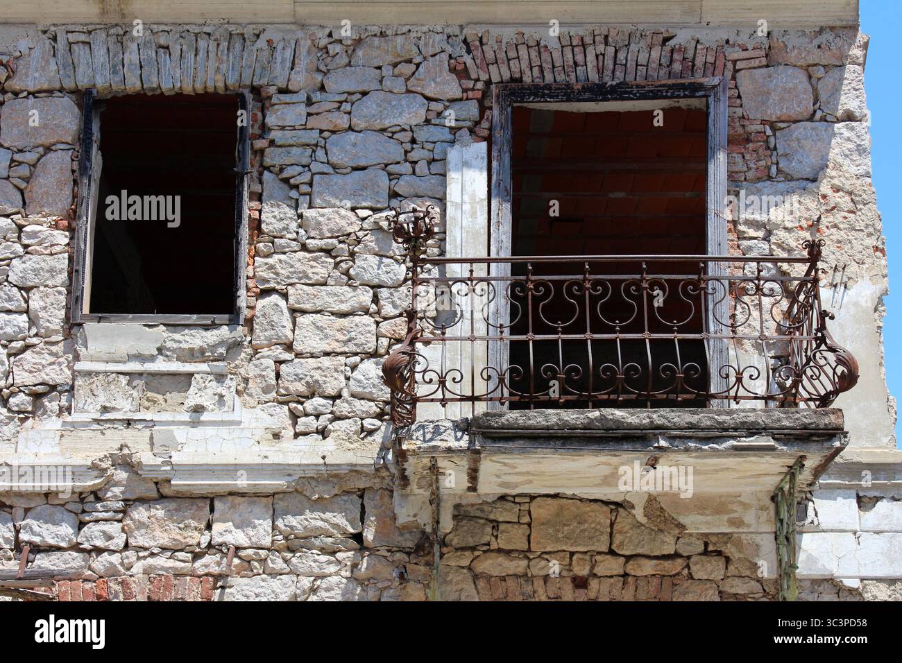 Un edificio in pietra resistente agli agenti atmosferici mostra finestre mancanti, muratura incrinata e ringhiere arrugginite del balcone, che illustrano il grave decadimento e l'abbandono strutturale Foto Stock