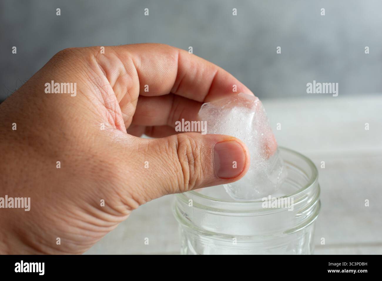 Vista di una mano che posiziona un cubetto di ghiaccio in un bicchiere da bere. Foto Stock