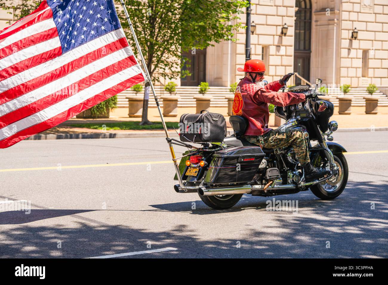 Washington D.C., USA, 25 maggio 2025. Un motociclista che indossa una giacca rossa del corpo dei Marines porta una grande bandiera americana durante un evento del Memorial Day. Foto Stock