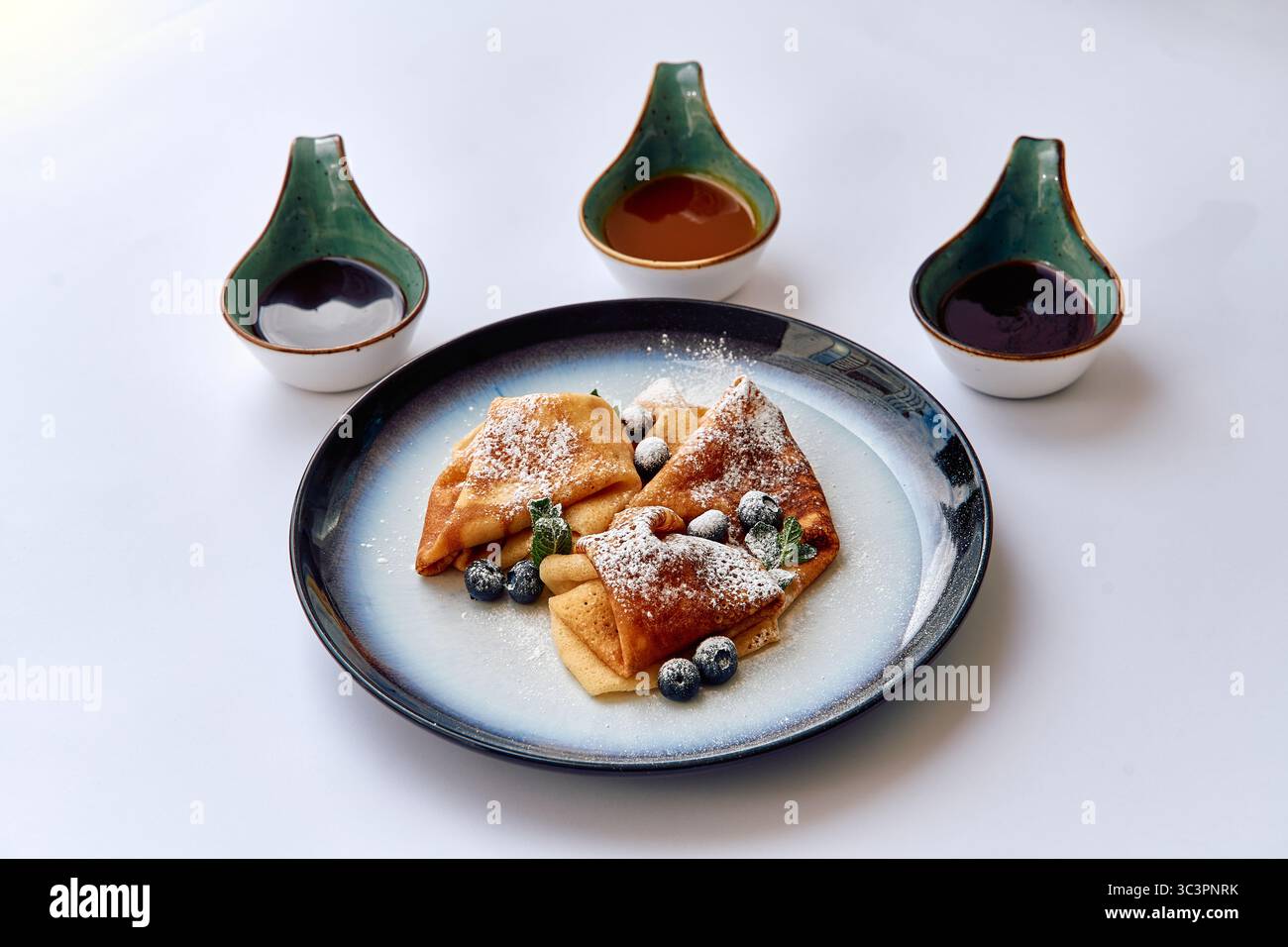 Un delizioso piatto di crepe ripieno di frutti di bosco freschi e spolverata di zucchero a velo accompagnato da tre salse per immersione Foto Stock