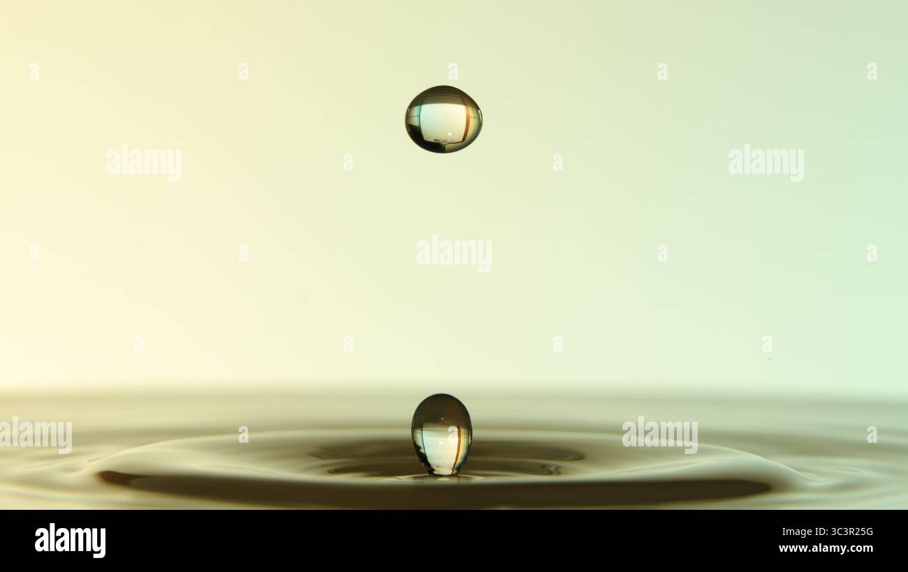 Primo piano di gocce d'acqua sospese su una superficie calma, che formano increspature e riflessi su sfondi a gradiente morbido. Foto Stock