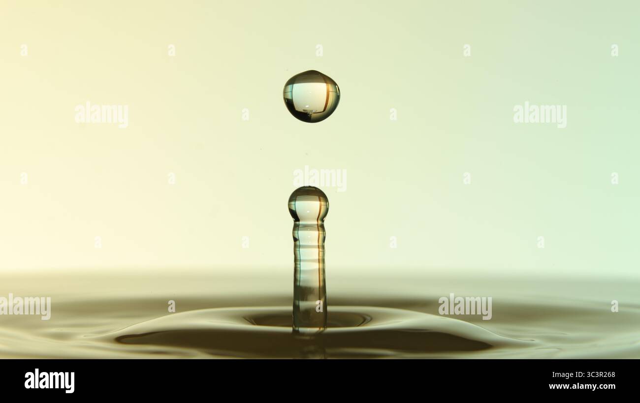 Primo piano di gocce d'acqua sospese su una superficie calma, che formano increspature e riflessi su sfondi a gradiente morbido. Foto Stock