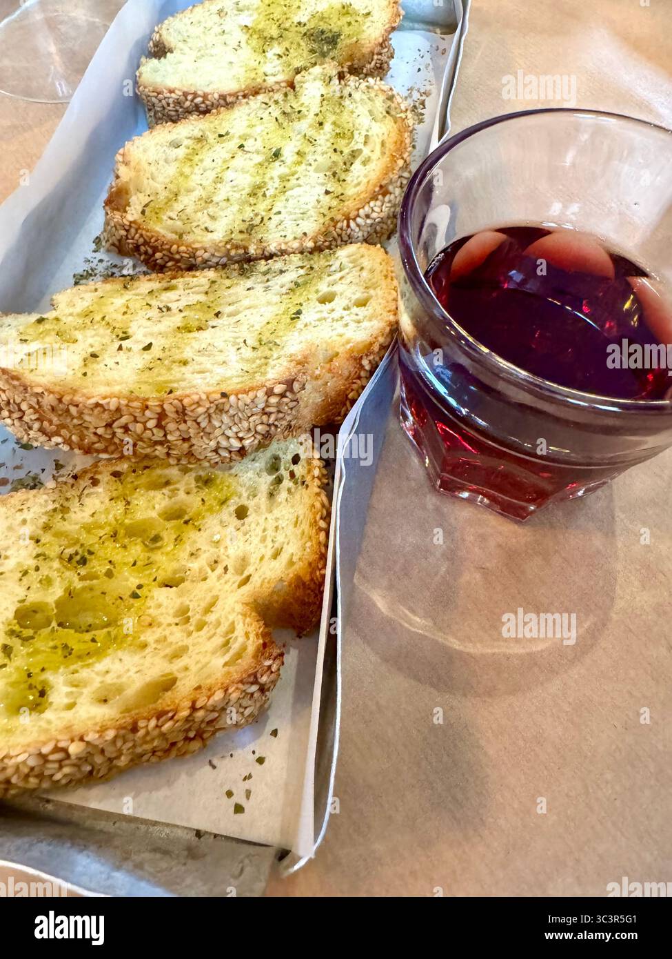 Tradizionale pane greco al sesamo con olio d'oliva ed erbe aromatiche servito con un bicchiere di vino rosso ad Atene, Grecia. Foto Stock