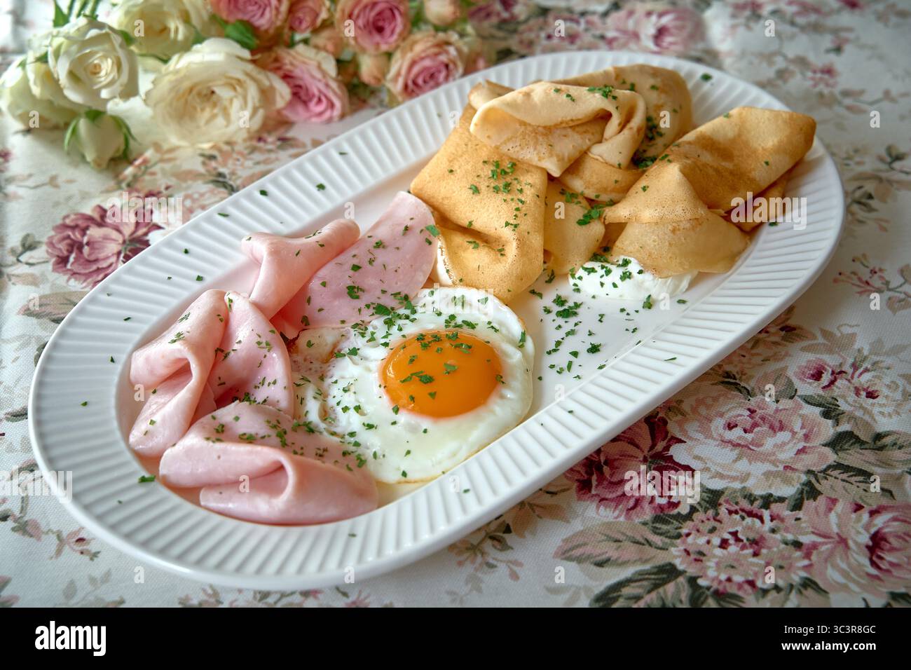 Un delizioso piatto con uova fritte, prosciutto salato e frittelle dorate adornate con erbe fresche, perfetto per una deliziosa colazione Foto Stock