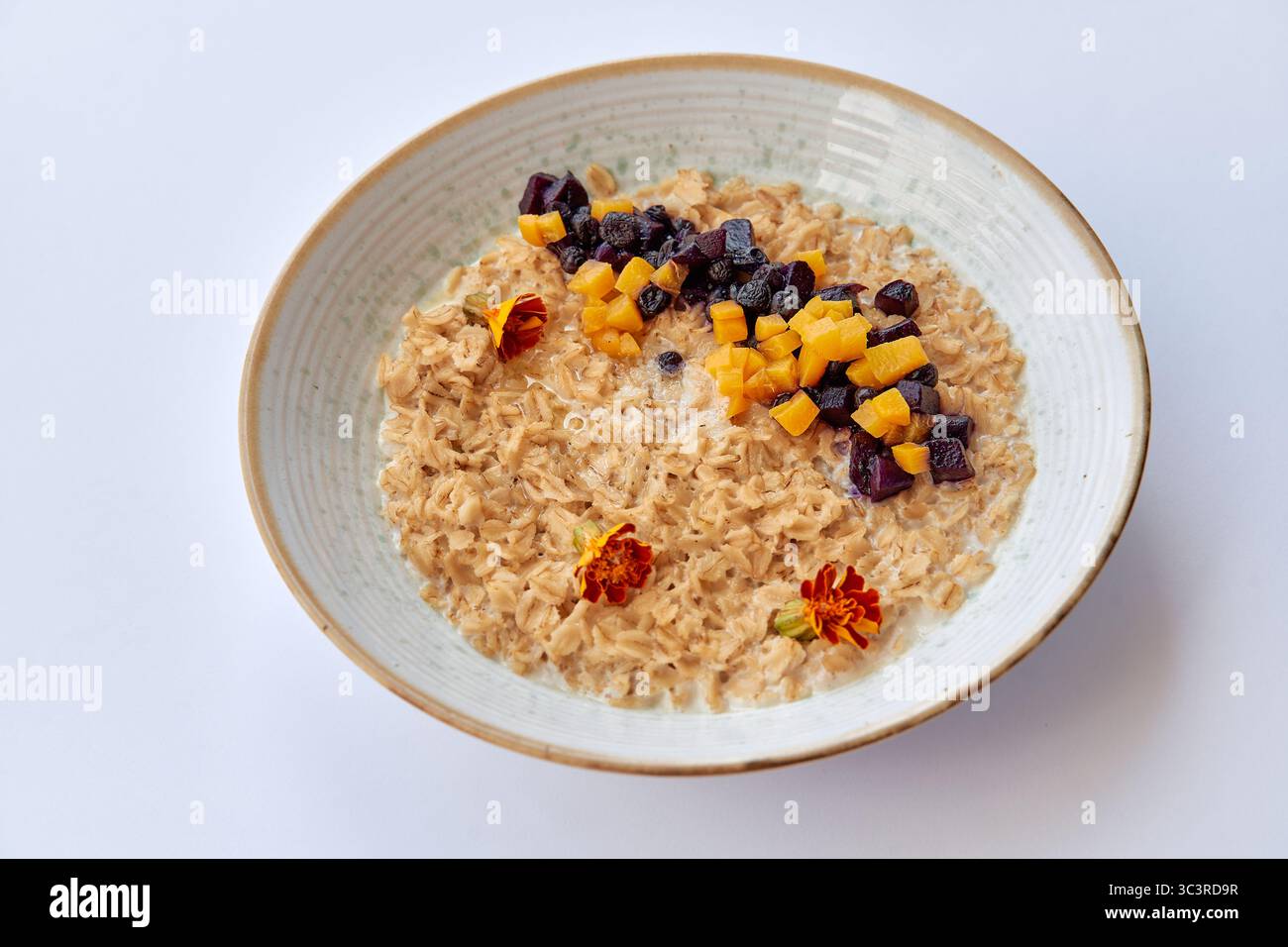 Deliziosa ciotola di farinata d'avena con frutta secca e fiori per una colazione nutriente Foto Stock