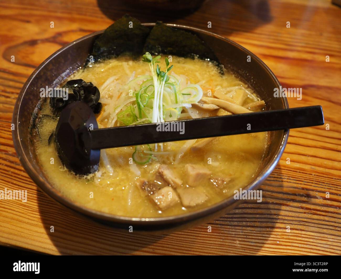Deliziosa zuppa tradizionale di noodle di ramen cotta con pasta di miso, carne, alghe e cipolla in una ciotola con cucchiaio di legno in Giappone Foto Stock