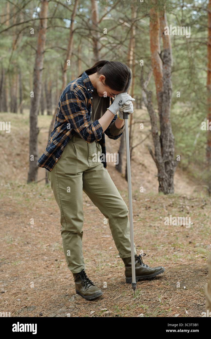 Giovane donna adulta che riposa mentre si appoggia al bastone da passeggio all'aperto Foto Stock