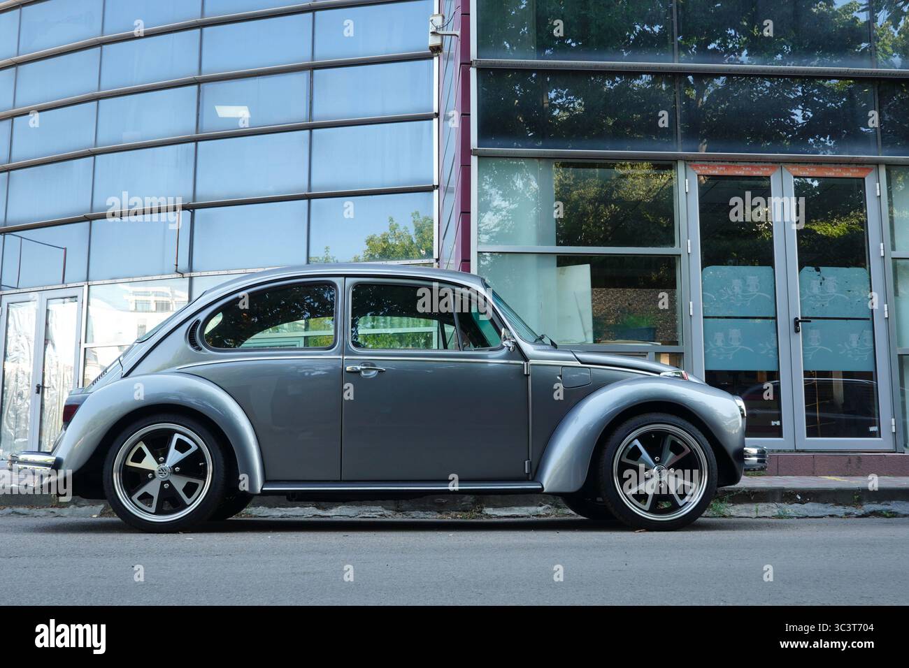Bucarest, Romania - 24 luglio 2025: Vista ravvicinata dell'auto d'argento Volkswagen Beetle retrò parcheggiata di fronte all'edificio in vetro dell'ufficio Foto Stock