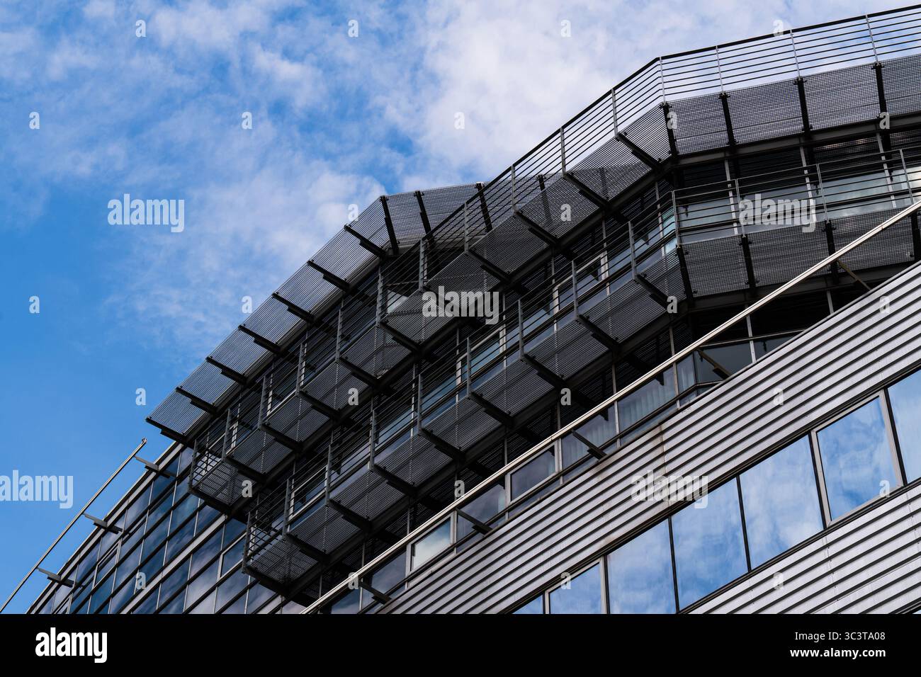 Moderna facciata di uffici con tende parasole angolate e pareti in vetro contro il cielo blu Foto Stock