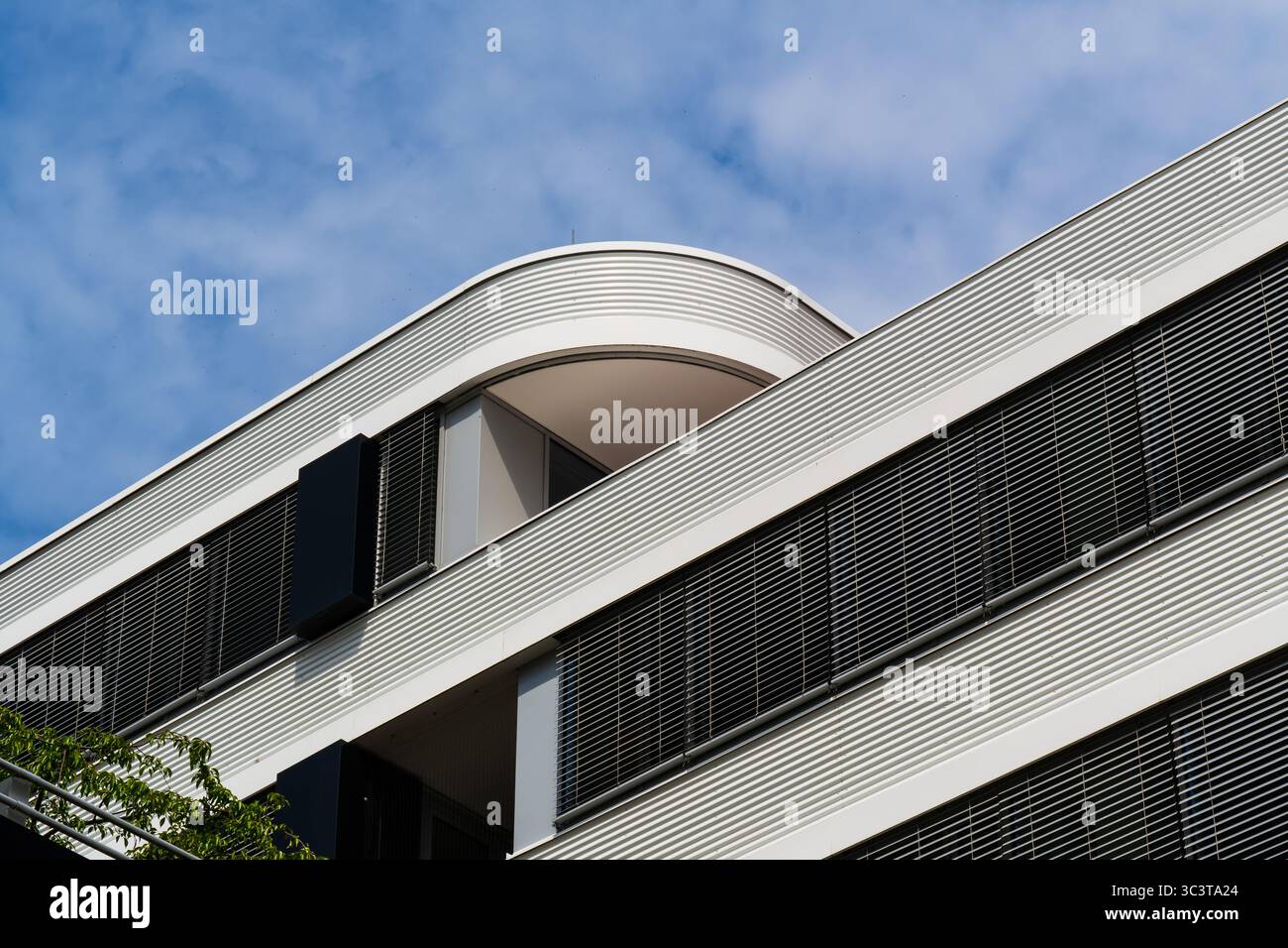 Facciata residenziale contemporanea con balconi bianchi curvi e tonalità ritmiche del sole Foto Stock