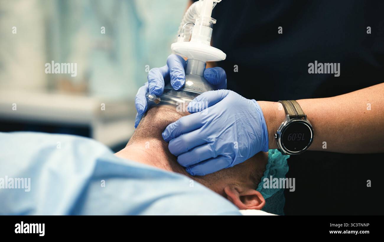 L'operatore sanitario con guanti blu sta fornendo anestesia a un paziente in un ambiente medico, evidenziando le pratiche sanitarie essenziali e il paziente Foto Stock