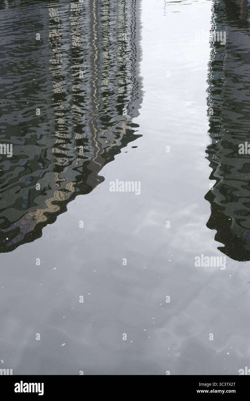 Grandi edifici di appartamenti che si riflettono sulla superficie di un fiume ondulato. Foto Stock