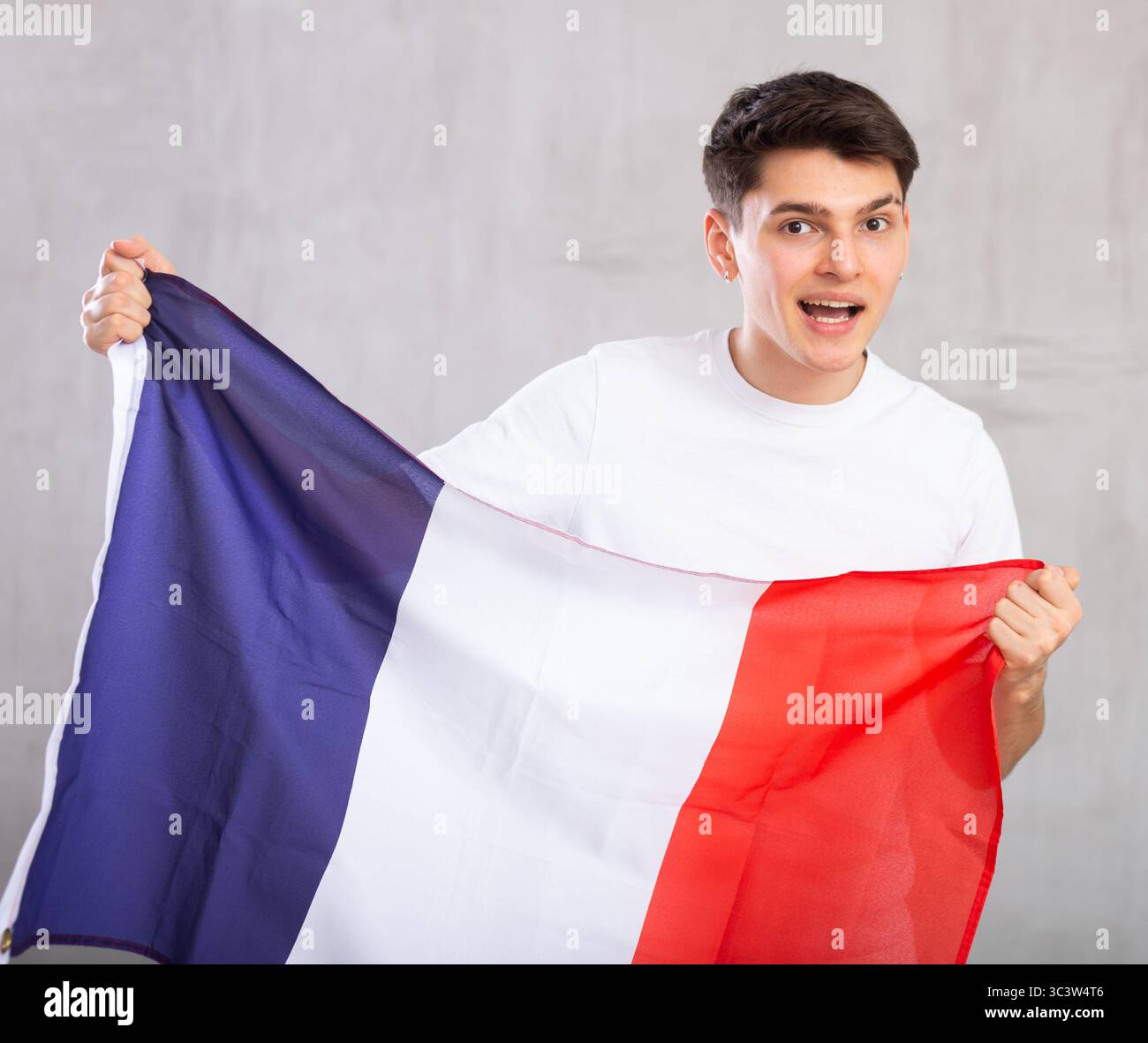 Eccitato, attivo spettatore maschile detiene bandiera nazionale della Francia in mani e canti slogan popolare Foto Stock