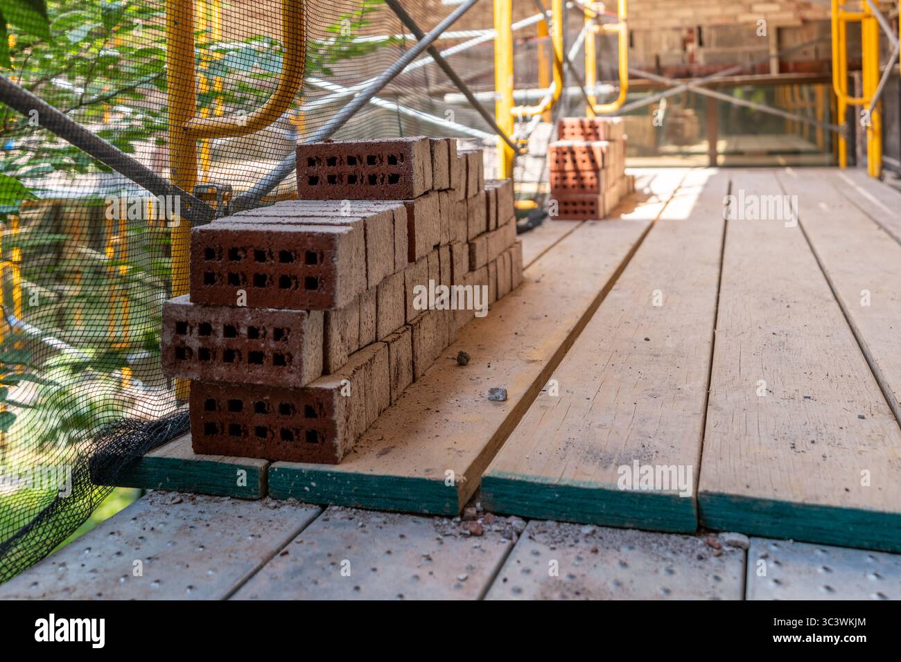 Vecchi mattoni impilati ordinatamente su impalcature in acciaio con pavimento in legno prima di essere reinstallati su un edificio esistente. Foto Stock